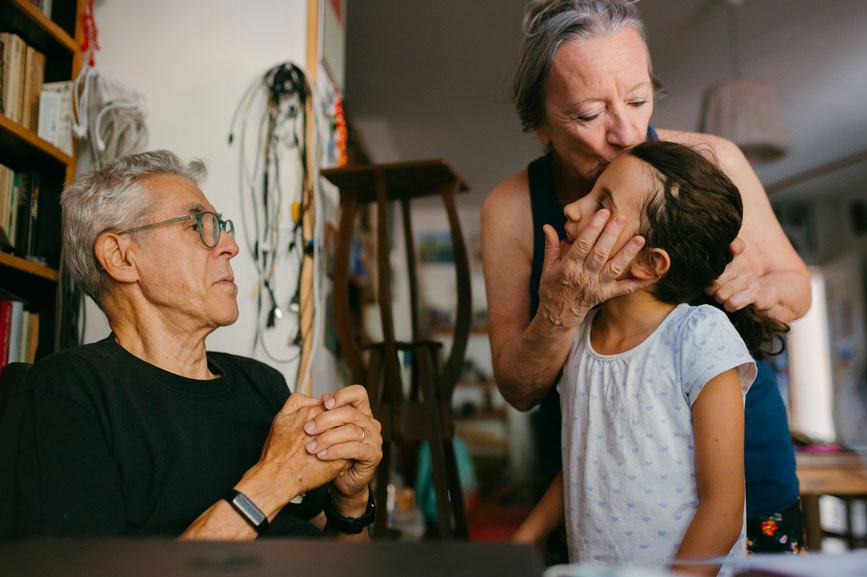 grandmother kissing the forehead of granddaughter with grandfather looking on